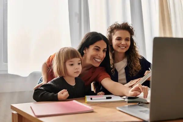 Due donne gioiose si impegnano con la figlia mentre lavorano su un computer portatile in un appartamento luminoso. — Foto stock