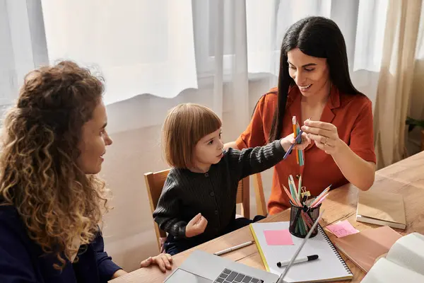 Two loving mothers engage with their daughter during a creative activity at home. — Stock Photo