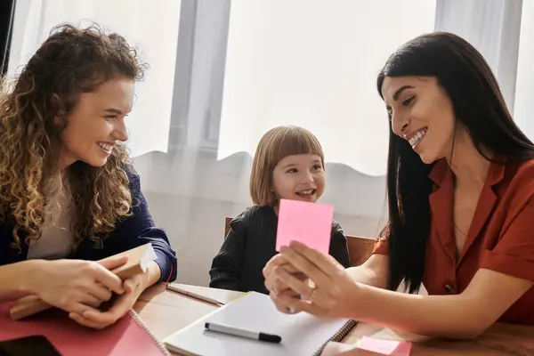 Due donne gioiose si impegnano con la loro giovane figlia in uno spazio luminoso e moderno pieno di calore. — Foto stock