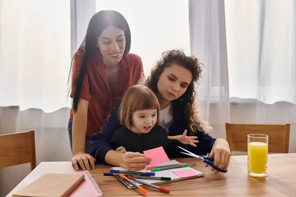 Two loving women guide their daughter as she crafts colorful creations in their cozy apartment. — Stock Photo