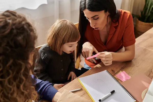 Due madri amorevoli condividono un momento gioioso con la loro figlia curiosa mentre siedono a un tavolo. — Foto stock