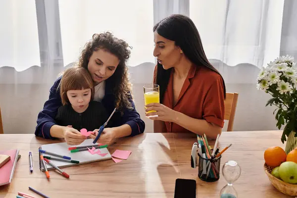 Two loving mothers engage with their daughter while crafting at a cozy table. — Stock Photo