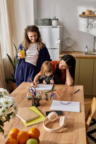 Due donne sostengono la loro figlia mentre disegna a un tavolo nel loro luminoso appartamento. — Foto stock