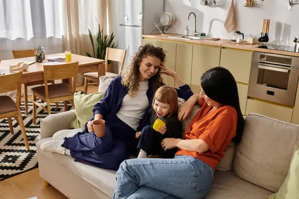 Two loving mothers share a joyful moment with their daughter in a cozy living space. — Stock Photo