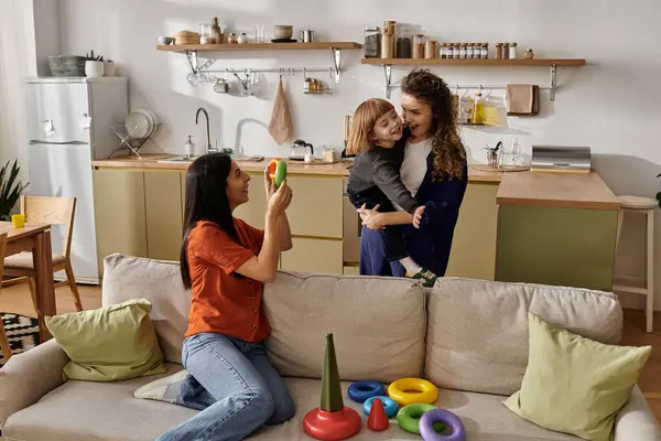 Two loving mothers share a joyful moment with their playful daughter at home. — Stock Photo