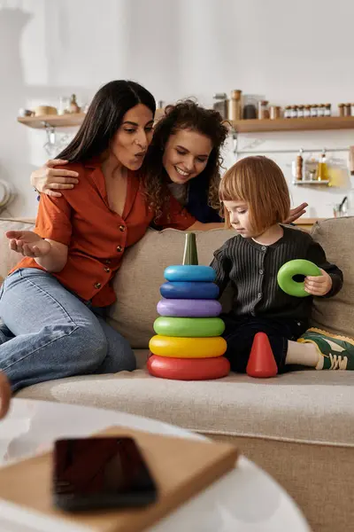 Two women joyfully build a tower of rings with their daughter. — Stock Photo