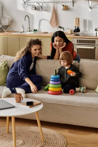 Two women guide their daughter as she plays with colorful stacking toys in a cozy living room. — Stock Photo