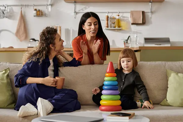 Two women engage in joyful conversation while their daughter plays with colorful stacking toys. — Stock Photo