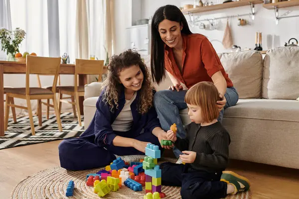 In a modern apartment, two women support their daughter as she builds with colorful blocks. — Stock Photo