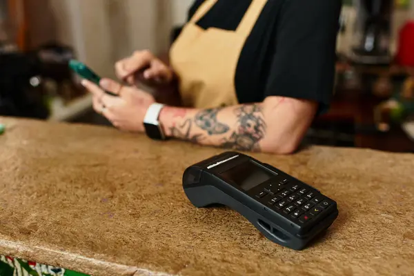 A young woman at a cafe is engaged in her phone while a payment device rests nearby on the counter. — Stock Photo