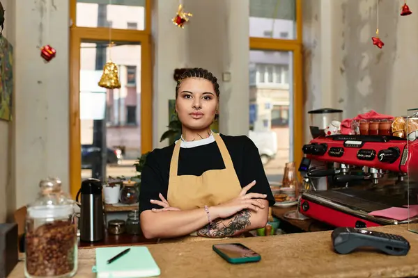 Eine junge Frau steht stolz hinter der Theke eines gemütlichen Cafés und zeigt ihre lebendige Persönlichkeit. — Stockfoto