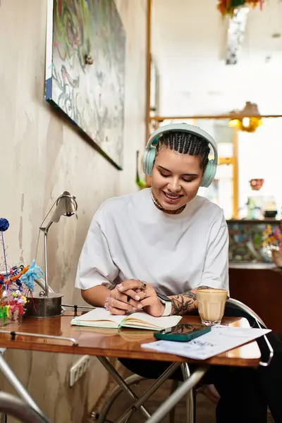 A beautiful young woman smiles while writing in her notebook at a vibrant cafe, lost in thought. — Stock Photo