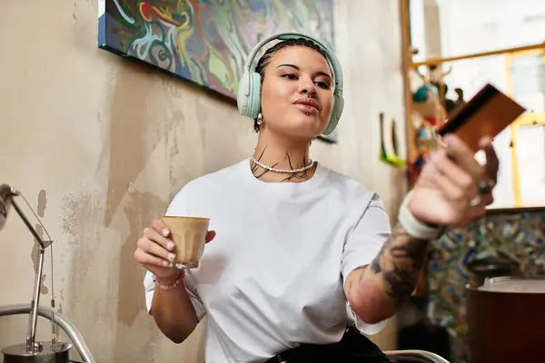 Una giovane donna in un caffè tiene un drink in una mano mentre usa il suo telefono, persa nel pensiero. — Stock Photo