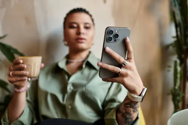 A young woman sits comfortably in a cozy cafe, sipping coffee and engaging with her smartphone. — Stock Photo