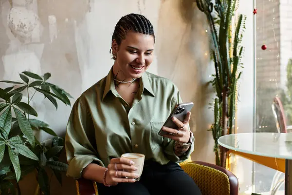 Smiling young woman sips coffee while browsing on her smartphone in a lively cafe. — Stock Photo