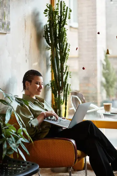 A young woman sits comfortably in a vibrant cafe, focused on her laptop amidst lush plants. — Stock Photo