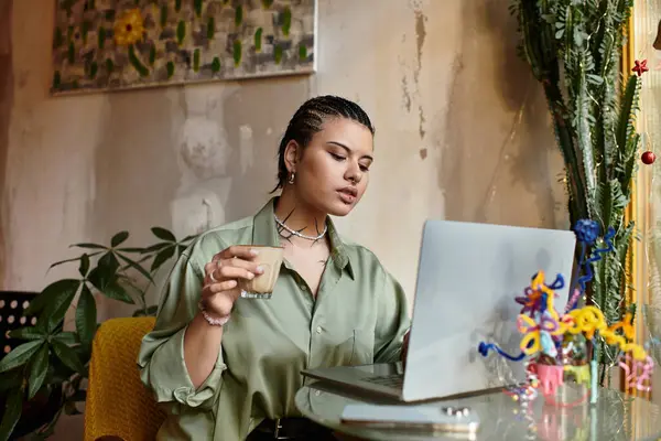 A young woman savors her drink and types thoughtfully on her laptop in a cozy cafe. — Stock Photo