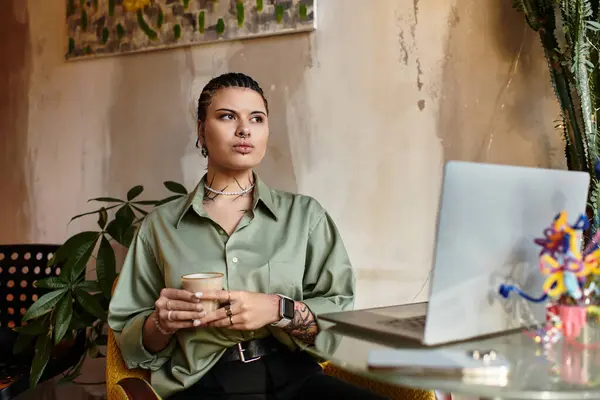A young woman sips coffee at a cafe, focused on her laptop amid greenery. — Stock Photo