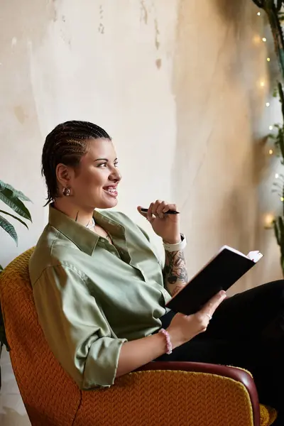 A young woman sits comfortably in a cafe, writing in her notebook with a cheerful expression. — Stock Photo