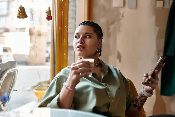 A young woman sits in a cafe, savoring her drink while engaging with her phone. — Stock Photo