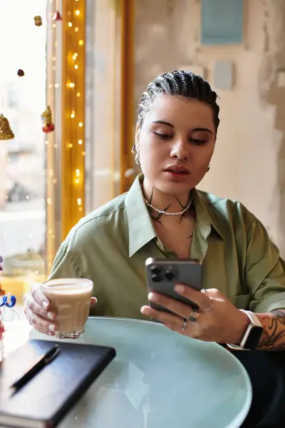 A charming young woman relaxes at a cafe, sipping her drink and on her phone. — Stock Photo