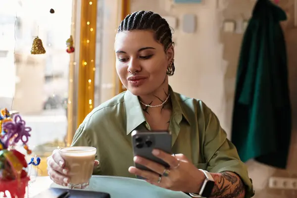 Una joven con una personalidad llamativa se deleita en una bebida caliente mientras navega por su teléfono. - foto de stock