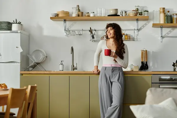 Sipping a hot beverage, a young woman relaxes in her bright and inviting kitchen space. — Stock Photo