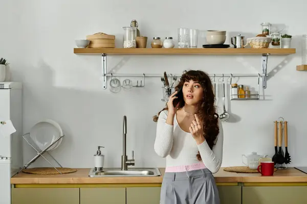 A young woman talks on the phone in a chic kitchen with elegant decor. — Stock Photo