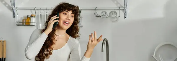 Une jeune femme joyeuse engage une conversation téléphonique animée tout en se tenant dans une cuisine élégante. — Photo de stock