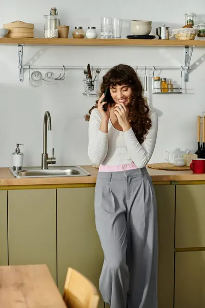 A young woman is smiling while speaking on the phone in her inviting kitchen. — Stock Photo