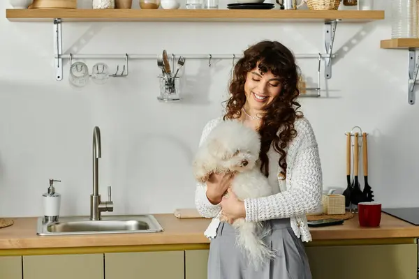 A young woman beams with joy while holding her fluffy dog in a stylish kitchen. — Stock Photo