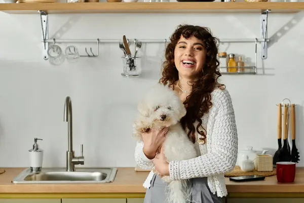 Smiling woman stands in a vibrant kitchen while cradling a small, fluffy dog. — Stock Photo