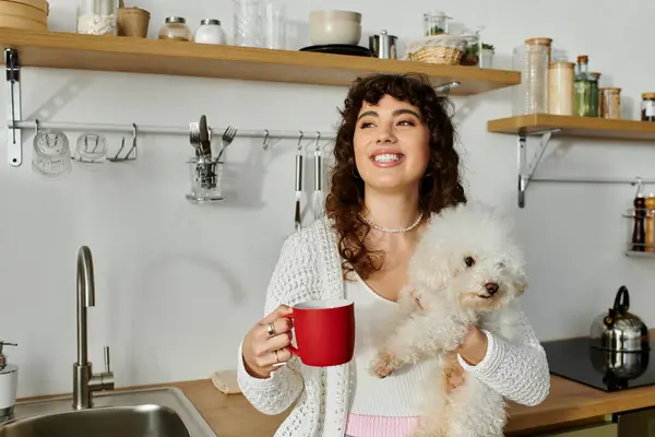 Sipping coffee and snuggling her fluffy dog, a young woman radiates warmth in a stylish kitchen. — Stock Photo