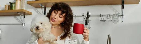 Cheerful woman hugs a small dog and sips a red mug, radiating warmth and joy. — Stock Photo