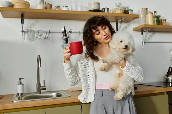 Bright kitchen setting featuring a young woman savoring coffee and cuddling her fluffy dog. — Stock Photo