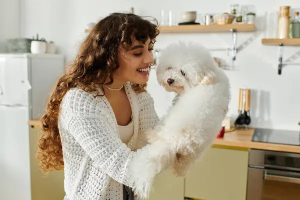 Embracing a moment of happiness, a young woman plays with a small white dog in a charming kitchen. — Stock Photo