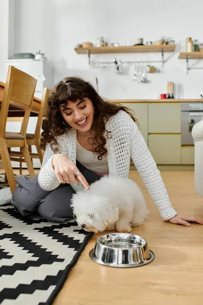 A young woman experiences happiness while engaging with her small dog in a stylish kitchen area. — Stock Photo