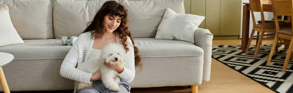 A young woman cuddles her small dog on a stylish sofa, radiating warmth and joy. — Stock Photo