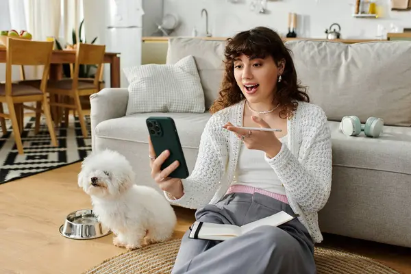 A young woman happily chats on her smartphone in a cozy living space with her dog. — Stock Photo