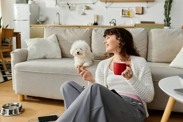 Young woman enjoys a relaxing time on the floor, sipping coffee with her playful dog nearby. — Stock Photo