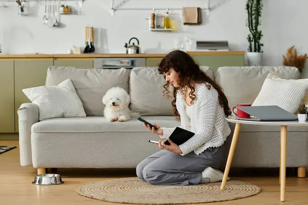 A young woman sits on the floor with her dog, focused on her mobile device. — Stock Photo
