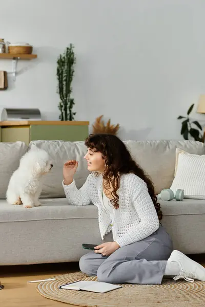 A young woman kneels on a soft rug, engaging playfully with her small fluffy dog in a warm home. — Stock Photo