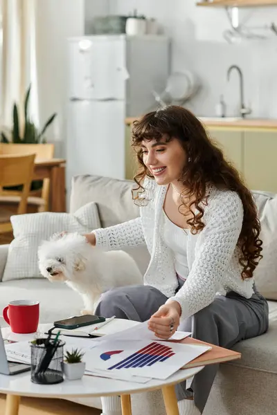 Junge Frau lächelt, während sie an ihren Projekten arbeitet und freudige Momente mit ihrem kleinen Hund teilt. — Stockfoto