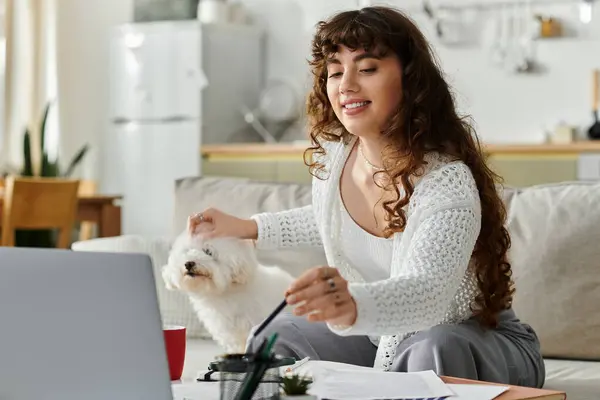 Bright and cheerful young woman pets her small dog while sitting at a stylish home workspace. — Stock Photo