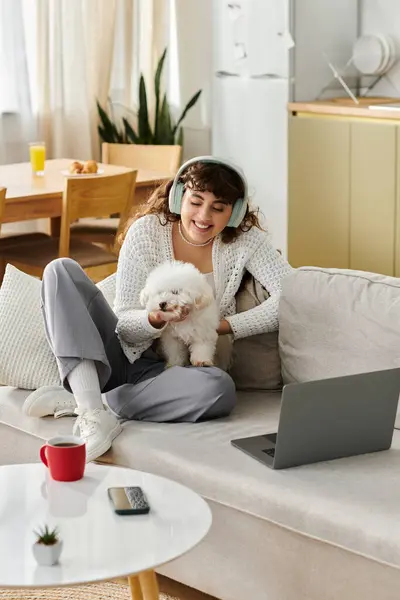 Cozy day indoors as a young woman interacts with her fluffy puppy and works on a laptop. — Stock Photo