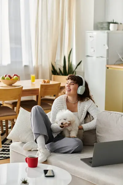 A young woman relaxes on a couch with headphones, cuddling her puppy in a cheerful room. — Stock Photo