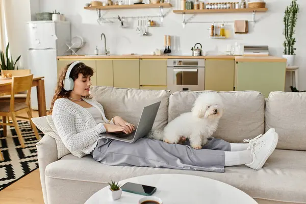 A woman enjoys her time working at home with her fluffy dog resting on her legs while she types. — Stock Photo