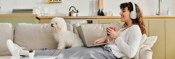 Relaxing in a comfortable living room, a young woman sips a warm drink and works on her laptop. — Stock Photo