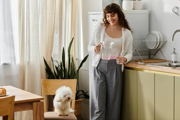 Una giovane donna con i capelli ricci versa una bevanda rosa come un cane soffice guarda con entusiasmo. — Foto stock