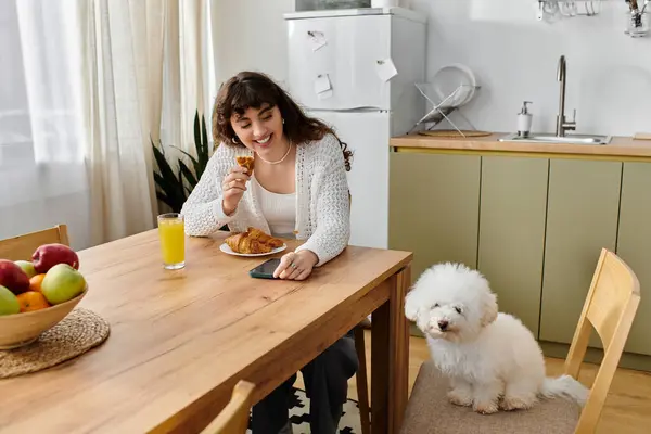 A young woman shares breakfast with her fluffy dog at a sunny wooden table. — Stock Photo